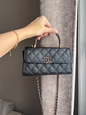 Svart quiltad handväska med kedja - Snygg svart handväska i quiltat mönster med guldfärgade detaljer och kedjehandtag. Väskan har ett elegant CC-spänne framtill och en lång axelrem i kedja och läder. Perfekt storlek för det viktigaste och ger en lyxig vibe till din outfit.