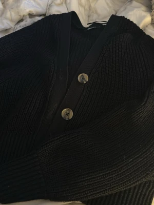 Svart stickad kofta med knappar - Mysig svart stickad kofta med stora knappar framtill. Perfekt att ha över en t-shirt eller topp för en avslappnad look. Långa ärmar och klassisk passform.