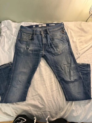 Replay jeans - Säljer ett par ljusblå jeans från Replay med slitningar och distressed detaljer på både fram- och baksida. Klassisk femficksmodell med läderpatch bak i midjan och raka ben. Perfekta för en avslappnad och trendig look.