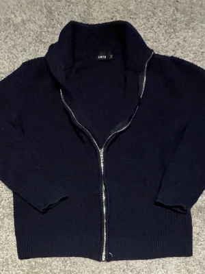 Svart stickad ziptröja från LMTD - Mysig svart stickad tröja från LMTD med dragkedja framtill och hög krage. Tröjan har långa ärmar och ribbade muddar vid ärmslut och nederkant. Perfekt för lager på lager och enkel att matcha med olika outfits.