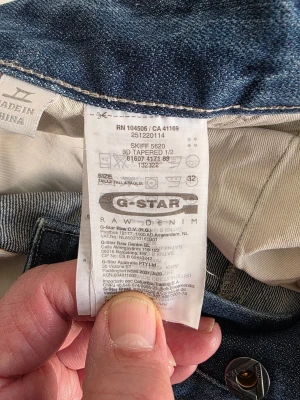 Blå jeansshorts från G-Star RAW - Säljer ett par blå jeansshorts från G-Star RAW med coola detaljer och stora fickor bak. Modellen är SKIFF 5620 3D Tapered och shortsen har en avslappnad passform med slitningar och knappar på fickorna. Perfekta för sommaren!