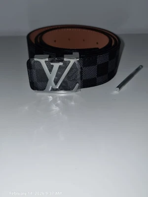 L.V bätle - Snyggt svart bälte från L.V med klassiskt rutigt mönster och stor L.Vi silver på spännet. Bältet har en stilren design och är gjort i skinn med en lyxig känsla. Perfekt accessoar för att lyfta din outfit.