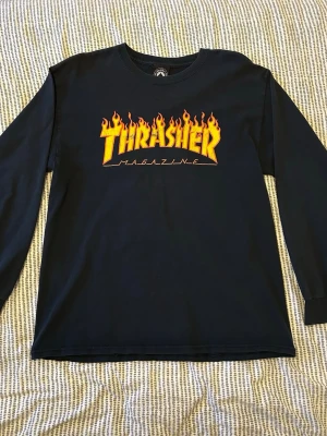 Svart långärmad Thrasher T-shirt  - Svart långärmad T-shirt från Thrasher med ikoniskt gult och orange flames-tryck på bröstet. Den är lite baggy på mig som är 174. Några enstaka hål på nedre ryggen, men annars i ganska gott skick.