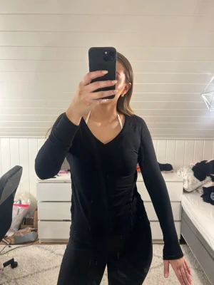 Svart långärmad träningströja från iciw - Svart långärmad träningströja med V-ringning. Sitter tight mot kroppen och är tillverkad i ett stretchigt material som passar perfekt för träning eller sportaktiviteter. Från iciw använt i flera år ändå i bra skick men säljes billigt för kan vara små defekter 