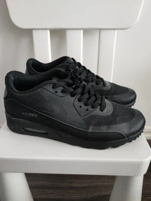 Nike Air Max helsvarta sneakers - Säljer ett par helsvarta Nike Air Max sneakers med klassisk siluett. Skorna har ovandel i mesh och syntet, samt den ikoniska Air Max-dämpningen i sulan. Snygga detaljer och diskret Nike-logga på sidan. Perfekta för dig som gillar stilrena och sportiga sneakers.