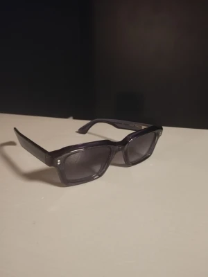 Svarta rektangulära solglasögon - Snygga svarta solglasögon ifrån chimi med rektangulära bågar och mörka glas. Klassisk och stilren design med breda skalmar och små silverdetaljer vid fronten. Perfekta för dig som vill ha en clean och modern look.