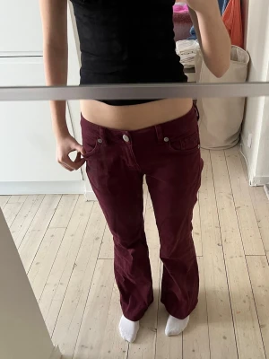 Vinröda Lågmidjade jeans  - Säljer ett par vinröda Lågmidjade jeans med bootcut-modell och låg midja. Byxorna har klassiska fem fickor och stängs med knapp och dragkedja. Perfekta för dig som vill ha en retro och trendig look med skön passform. Använt ett fåtal gånger 
