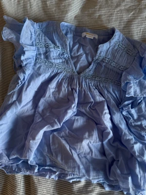 Ljusblå volangblus  - Supersöt ljusblå blus med volangdetaljer på ärmarna och broderade partier upptill. Blusen har v-ringning i fram💙