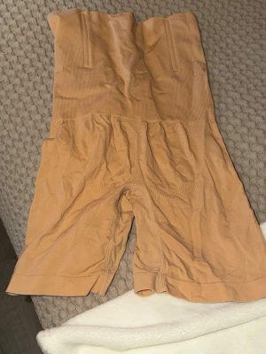 Beige shapewear med hög midja - Säljer ett par beige shapewear shorts med hög midja och sömlös design. De är tillverkade i ett stretchigt material som formar och slätar ut siluetten. Perfekt under outfits.