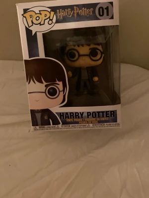 Harry Potter Pop! Vinylfigur 01 - Säljer en Pop! vinylfigur av Harry Potter från Funko, nummer 01. Figurerna är kända för sina stora huvuden och detaljerade design. Den här figuren har Harrys klassiska glasögon, trollstav och Hogwarts-uniform. Perfekt för samlare eller Harry Potter-fans.