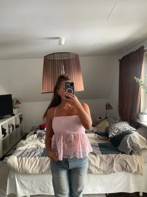 Ljusrosa spetslinne med volang - Supersöt ljusrosa linnetopp med tunna axelband och volang nertill. Toppen är i spets med fina broderade detaljer och har öppen rygg. Aldrig använd.