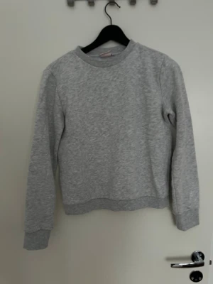 Grå basic sweatshirt  - En enkel och stilren grå sweatshirt med rund hals och långa ärmar. Tröjan har ribbade muddar vid ärmslut och nederkant. Perfekt för en avslappnad och bekväm look. Materialet känns mjukt och passar till det mesta.