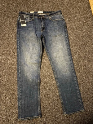 Mörkblå regular jeans Jack & Jones nyköpt aldrig använda  - Klassiska mörkblå jeans från Jack & Jones i modellen JJICLARK JJORIGINAL. Jeansen har rak passform och normal midja, med subtila slitningar och kontrastsömmar. 
