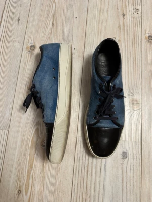 Lanvin sneakers - Uk 11 i storlek. Snygga blå lanvin med svart tå i glansigt material. Skorna har blå snörning och vit sula och material i mocka. Perfekta för dig som gillar en stilren men unik look. Prisförändring och frågor uppskattas. 