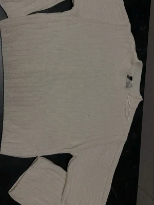 Beige ribbstickad tröja - Säljer en beige ribbstickad tröja med rund hals och långa ärmar. Tröjan har en enkel och stilren design med diskreta vertikala ränder i stickningen. Perfekt för dig som gillar en clean och avslappnad look. Lite nopprig 