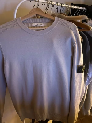 Beige  tröja från Stone Island - Säljer en beige tröja från Stone Island med rund halsringning och ribbade detaljer vid axlar, ärmslut och nederkant. Tröjan har den klassiska Stone Island-loggan på vänster ärm. Perfekt för dig som gillar stilrena plagg med streetwear-vibe.