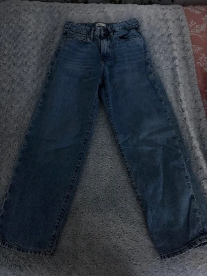 Blå raka jeans  - Säljer ett par klassiska blå jeans från gina med rak passform och hög midja. Jeansen har fem fickor och bälteshällor, tillverkade i robust denim. Perfekta för en avslappnad och trendig look.