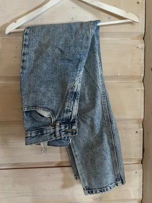 Blå vintage raka jeans - Ett par klassiska blå vintage jeans med rak passform och hög midja. Jeansen har en tvättad look med ljusa partier och slitna detaljer vid benslut och fickor. Perfekta för en avslappnad och trendig stil.