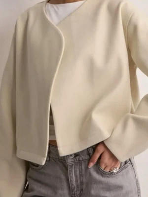 Beige croppad jacka med unik skärning - Trendig beige jack med croppad passform och snygg asymmetrisk skärning framtill. jackan har långa ärmar och är tillverkad i ett mjukt, slätt material. 