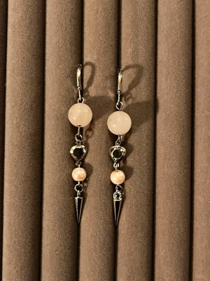 Långa örhängen med pärlor och metallspets - Säljer ett par långa örhängen med ljusrosa pärlor, hjärtformad metall och spetsiga silverfärgade detaljer. Örhängena har en cool mix av mjuka pärlor och edgy metallspetsar, perfekta för dig som gillar statement-accessoarer.