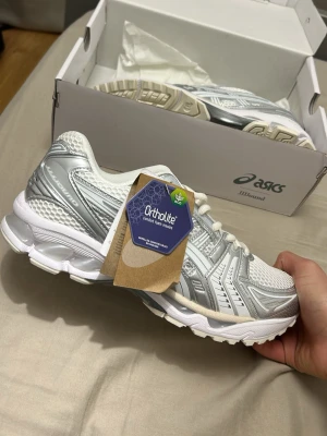 ASICS x JJJJound vita sneakers - Snygga vita och silverfärgade sneakers från ASICS i samarbete med JJJJound. Mycket stilrena skor som funkar till alla årstider, ifall du är en person som vill ta mode till ny nivå så är detta precis vad du behöver. Asics är inne och ni bör va snabba på detta priset, med ett generöst pris på 1299 så får du en top deal!