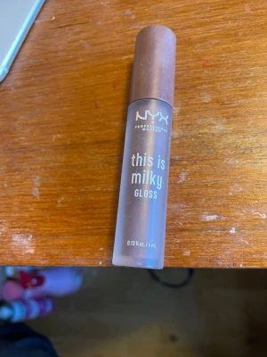 NYX This Is Milky Gloss brun - NYX This Is Milky Gloss i en mjölkigt brun nyans. Läppglanset kommer i en smidig tub med skruvlock och har en mjuk applikator. Ger en glansig finish och känns återfuktande på läpparna. Perfekt för dig som gillar naturliga, mjuka färger.