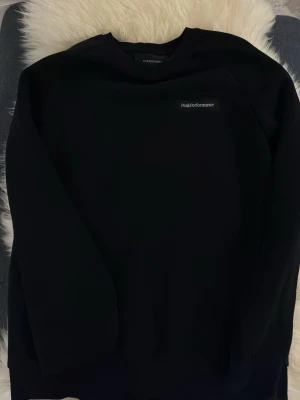 Svart sweatshirt Peak Performance - En stilren svart sweatshirt från Peak Performance med diskret logga på bröstet. Klassisk rund halsringning och mjukt material som känns skönt mot huden. Perfekt till jeans eller joggers för en avslappnad look.
