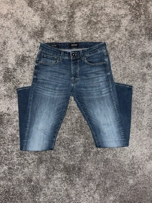 Blå slim fit jeans från Jack & Jones  - Snygga blå slim fit jeans från Jack & Jones med klassisk femficksdesign och lätt slitna detaljer framtill. Jeansen har normal midja och är tillverkade i stretchigt denim för extra komfort. Perfekta för en avslappnad och trendig look.