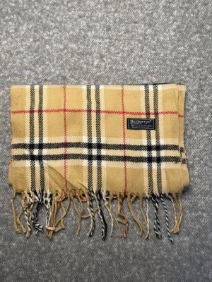 Beige rutig halsduk från Burberrys - Klassisk beige halsduk från Burberrys med ikoniskt rutmönster i svart, vitt och rött. Tillverkad i 100% lammull och har fransar i ändarna. Perfekt accessoar för att lyfta din outfit med en tidlös brittisk stil. Originaletikett, Made in England