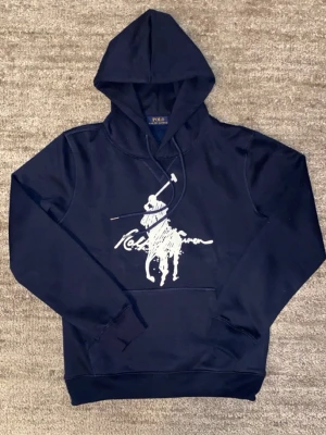 Marinblå hoodie från Polo Ralph Lauren - Riktig fet hoodie från Polo med tryck på framsidan. Helt ny, vid frågor är de bara skriva.