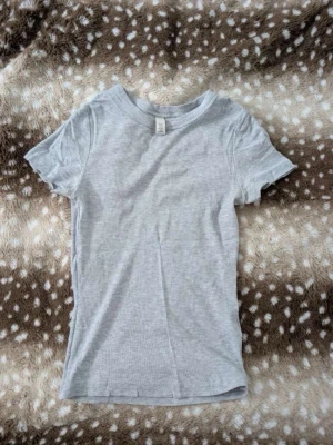 Ljusgrå basic t-shirt - En enkel ljusgrå t-shirt i mjuk bomull med rund hals och korta ärmar. Perfekt till jeans eller shorts för en avslappnad look. Klassisk passform och diskret design utan tryck eller mönster.