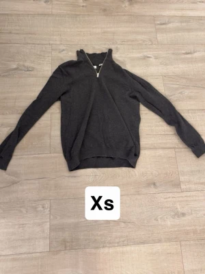 Mörkgrå halvzip tröja XS - Mörkgrå tröja med halv dragkedja i halsen och långa ärmar. Tröjan har ribbade muddar vid ärmslut och nederkant. Perfekt för lager på lager och enkel att matcha med olika outfits.
