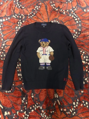 Mörkblå Polo Ralph Lauren Teddy Bear stickad tröja - Stickad mörkblå tröja från Polo Ralph Lauren med baseball Teddy Bear tryck på bröstet. Säljer pga blivit lite för liten för mig (182 cm). Storlek L (14-16 år) men sitter som XS-S ungefär.  Skick 9/10 använd endast ett fåtal gånger. Köpt ny för strax över 2500kr  Tveka inte att höra av er vid fler frågor om passform eller likande!