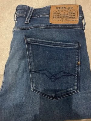 Mörkblå jeans från Replay - Snygga mörkblå jeans från Replay med klassisk femficksmodell och raka ben. Jeansen har en läderpatch med Replay-logga bak i midjan och diskreta slitningar för en cool look. Tillverkade i mjuk denim med stretch för extra komfort.