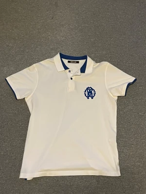  Roberto Cavalli - Vit pikétröja från Roberto Cavalli med blå detaljer på krage och ärmslut samt blå logga broderad på bröstet. Är i storlek L men passar även M