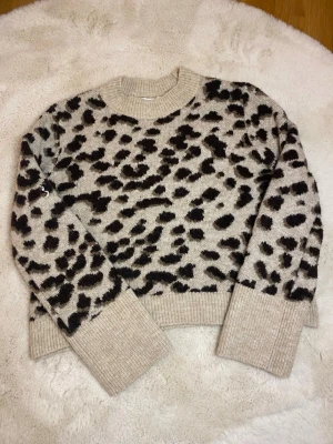 Var snabb!Beige leopardmönstrad stickad tröja H&M - Stickad tröja från H&M i beige med svart leopardmönster. Tröjan har rund halsringning, långa ärmar och breda ribbade muddar vid ärmslut och nederkant. Perfekt för dig som gillar djurmönster och vill ha en trendig look.