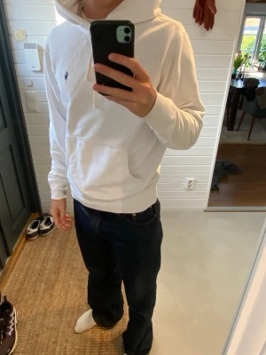  Ralph Lauren hoodie  - Vit hoodie från Polo Ralph Lauren med klassisk huva och broderad logotyp på bröstet. Tröjan har en stor magficka och ribbade muddar vid ärmslut och nederkant. Perfekt för dig som gillar stilren och enkel design.