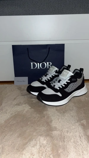 Dior b25 - Snygga chunky sneakers i svart och vitt med tjock vit sula. Ovandelen har meshdetaljer i grått och svart samt partier i mockaimitation. Skorna har vita skosnören och en sportig vibe som passar till streetwear.