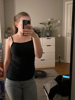 Svart linne med smala axelband - Snyggt svart linne med smala axelband och rak halsringning. Perfekt att matcha med jeans eller kjol. Enkel och stilren design som passar till många olika looks. OBS! Linnet är köpt från H&M barnavdelning och är i storlek 14y+ vilket är 170. Storlek 34-36