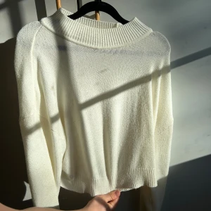 Vit stickad tröja med bred krage - Säljer en stilren vit stickad tröja med bred ribbad krage och långa ärmar. Tröjan har en avslappnad passform och ribbade muddar vid ärmslut.