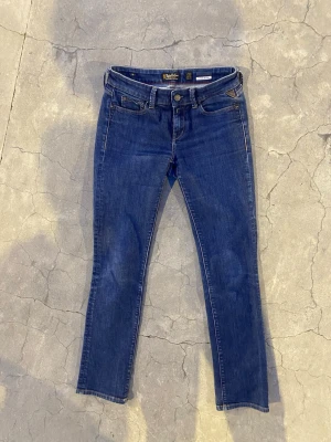Blå skinny jeans från Replay - Snygga blå skinny jeans från Replay med klassisk femficksmodell och guldfärgade detaljer. Jeansen har normal midja och är tillverkade i ett mjukt denimtyg. Stilsäker passform som funkar till det mesta och cool Replay-logga på fickan.