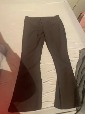 Bruna utsvängda kostymbyxor - Säljer ett par bruna kostymbyxor med utsvängda ben och hög midja. Byxorna har klassisk design utan synliga fickor framtill och stängs med dold knapp och dragkedja. Perfekta för en stilren och trendig look.