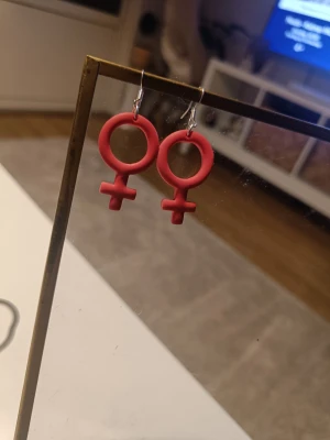 Rosa örhängen i kvinnosymbol-form - Unika örhängen i form av kvinnosymboler, tillverkade i rosa polymerlera. Hängande modell med silvriga krokar. Perfekt accessoar för att uttrycka din stil och statement. Snygga och trendiga örhängen som verkligen sticker ut. Strass! 