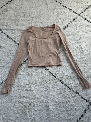 Beige croppad långärmad topp - Snygg beige croppad topp med långa ärmar och rundad urringning. Tillverkad i ett mjukt och tunt material som känns skönt mot huden. Perfekt att styla med jeans eller kjol för en trendig look.