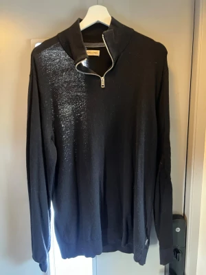 Svart stickad tröja med halv dragkedja - Svart stickad tröja från Jack & Jones med hög krage och halv dragkedja framtill. Tröjan har långa ärmar och ribbade muddar vid ärmslut och nederkant. Perfekt för lager på lager och enkel att matcha med olika outfits.