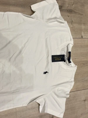 Vit t-shirt från Polo Ralph Lauren - Klassisk vit t-shirt från Polo Ralph Lauren med den ikoniska broderade loggan i marinblått på bröstet. T-shirten har rund halsringning och korta ärmar. Tillverkad i mjuk bomull för en skön och avslappnad känsla.