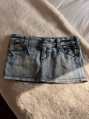 Blå jeansminikjol med nitar - Säljer en jätte fin jeanskjol som är perfekt nu till sommaren. Säljer då den tyvärr är alldeles för stor för mig. 