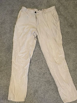 Beige linnebyxor raka ben - Säljer ett par ljusbeige linnebyxor med raka ben och klassisk passform. Byxorna har knapp och dragkedja framtill samt sidofickor. Perfekta för en avslappnad och stilren look. Materialet är svalt och luftigt linne.