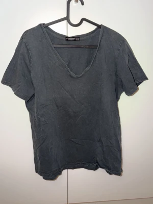 Mörkgrå v-ringad t-shirt Stradivarius - En enkel och stilren mörkgrå t-shirt från Stradivarius med v-ringning och korta ärmar. Tillverkad i mjuk bomull som känns skön mot huden. Perfekt till jeans eller shorts för en avslappnad look.