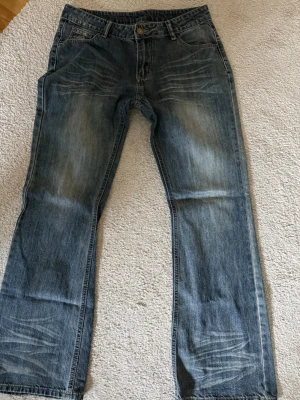 Blå bootcut jeans med slitningar - Säljer ett par blå jeans med raka ben och snygga slitningar på enden. Jeansen har klassisk femficksmodell och en tvättad look med ljusare partier. Perfekta för en avslappnad och trendig stil.